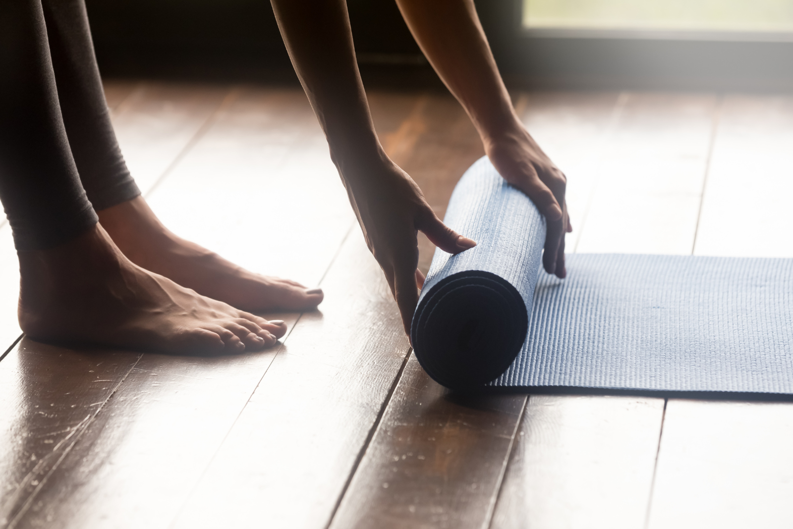 person rolling yoga mat on a hardwood floor barefoot