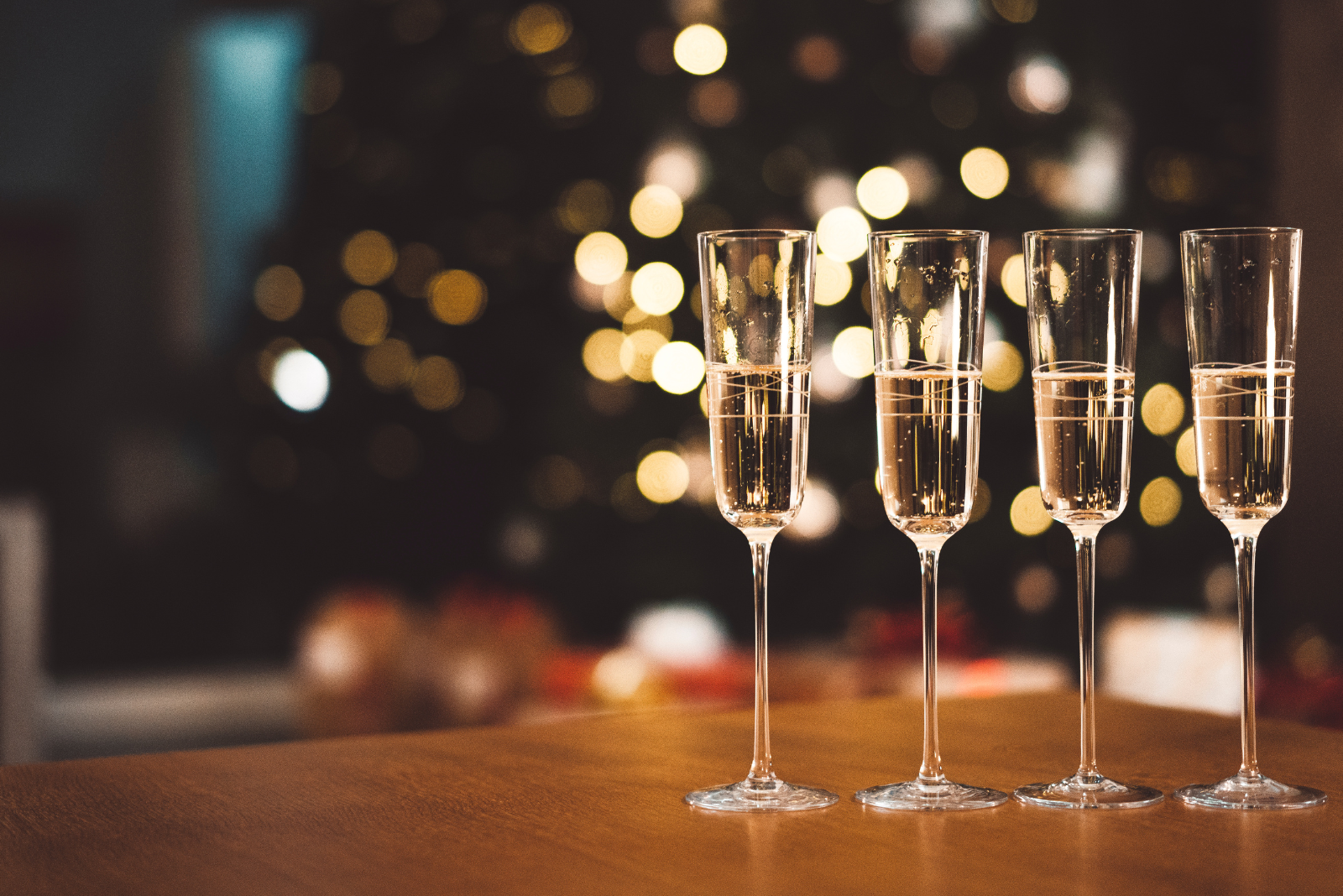 four champagne flutes with champagne in front of a holiday tree