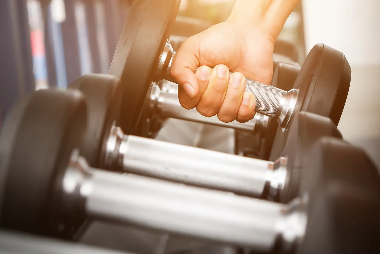 hand picking up a dumbell from a dumbell rack