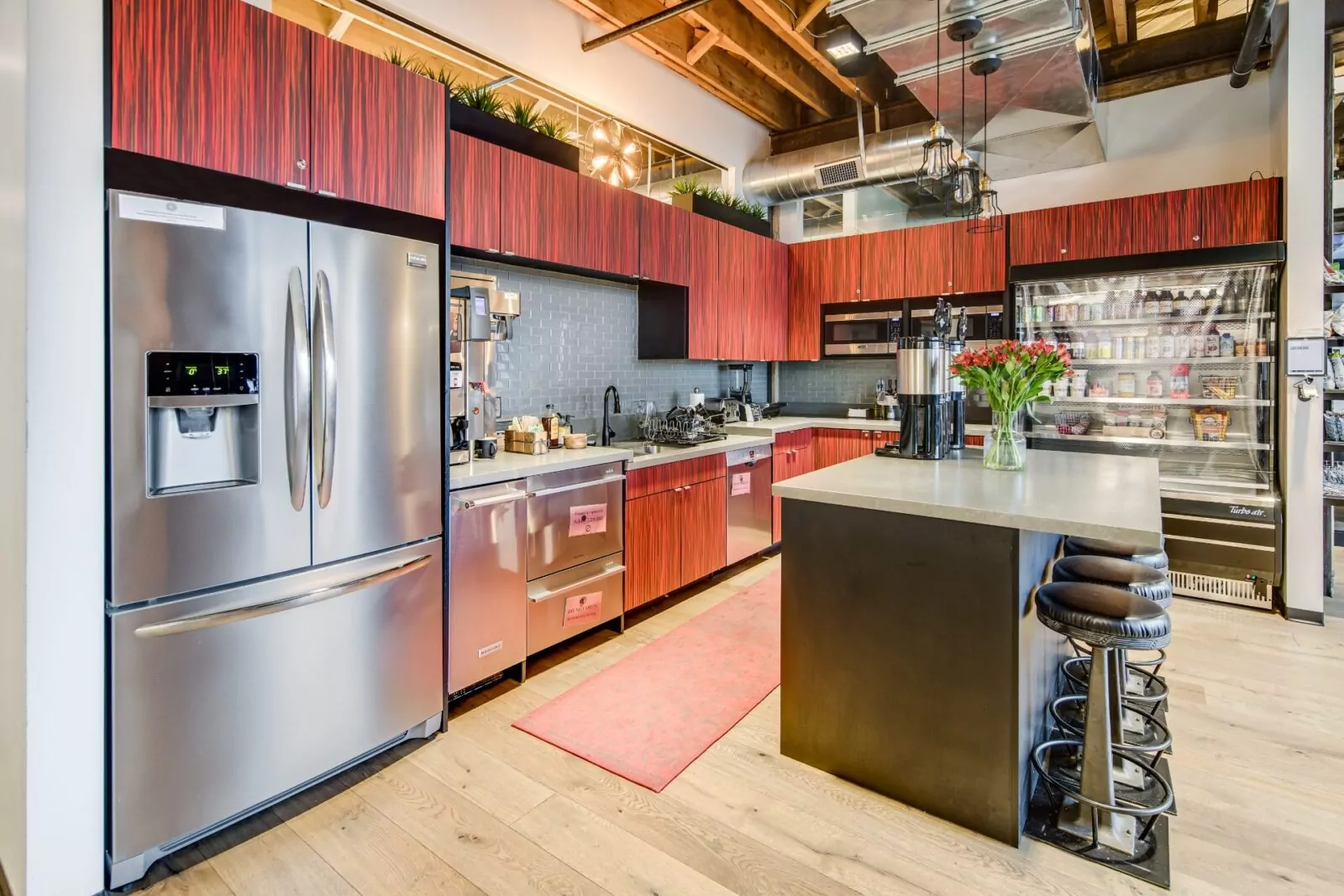 Modern communal kitchen at Shift Workspaces featuring stainless steel appliances, a spacious island, and warm wood cabinetry