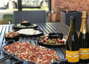 Charcuterie board, bruschetta, and bottles of cava set up for an outdoor gathering at Shift Workspaces Denver and Littleton.