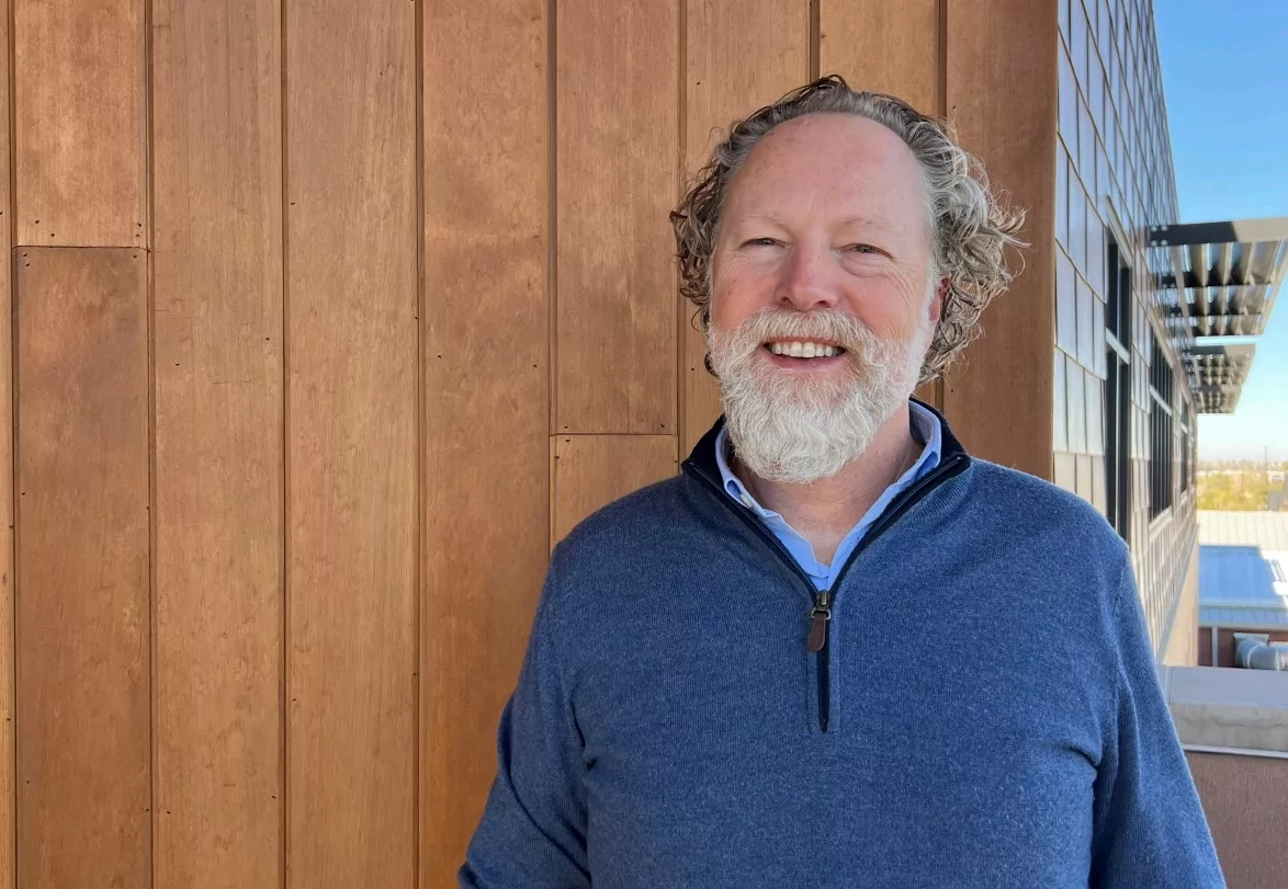 Professional headshot of Elliott Lowe from Timberline Agency wearing a blue sweater with a neutral background.