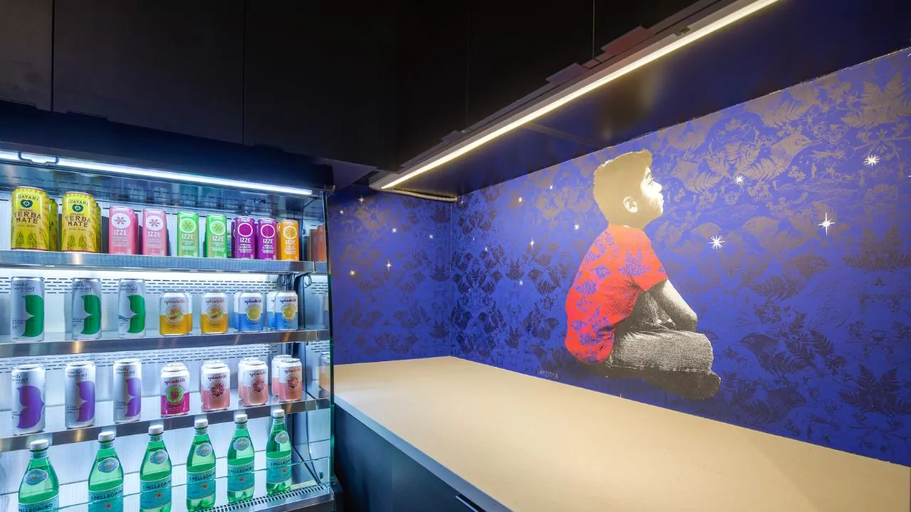 Shift Workspaces refreshment area with a stocked beverage fridge and vibrant wall mural featuring a child gazing at the stars