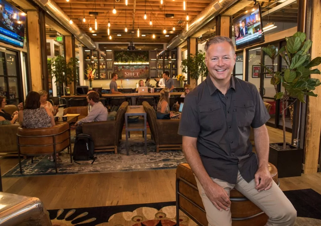 Grant Barnhill at Shift Workspaces, seated in a stylish coworking lounge with warm lighting, modern decor, and a vibrant community atmosphere