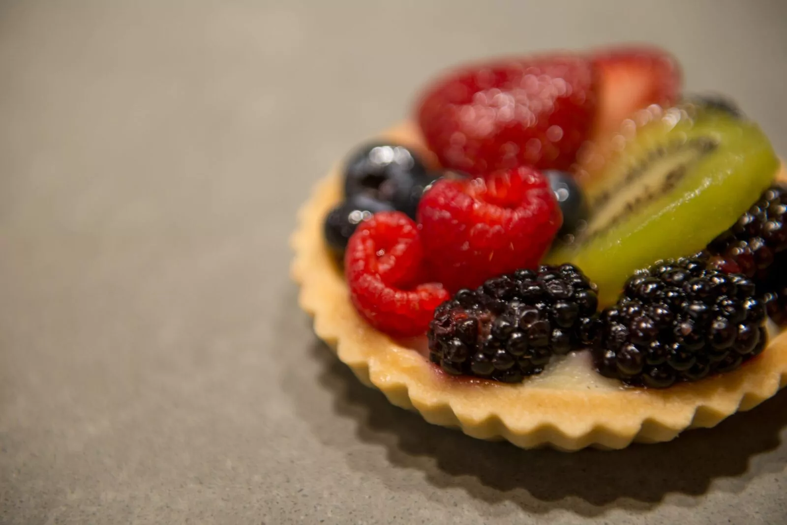 Close-up of a fresh fruit tart with raspberries, blackberries, blueberries, kiwi, and strawberries on a golden crust
