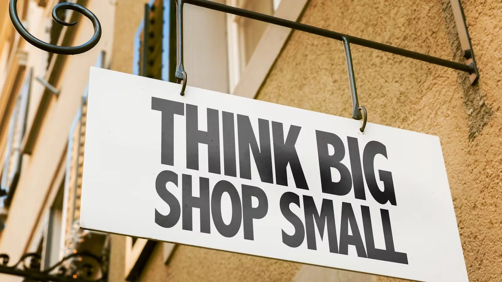 White sign with bold black text reading "Think Big Shop Small" hanging near Shift Workspaces Denver and Shift Littleton.
