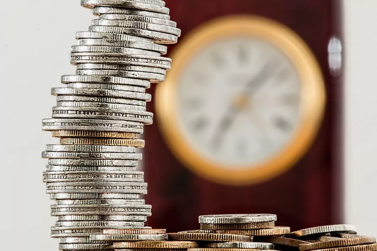 Stack of silver and gold coins with a blurred clock in the background at Shift Workspaces Denver and Littleton